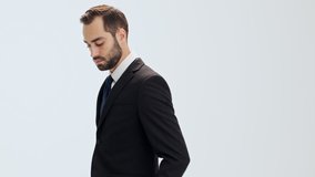 Pensive young businessman in black suit and blue tie raising his head and becoming happy while looking at the camera over gray background isolated