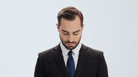 Serious young businessman in black suit and blue tie raising his head and looking at the camera over gray background isolated