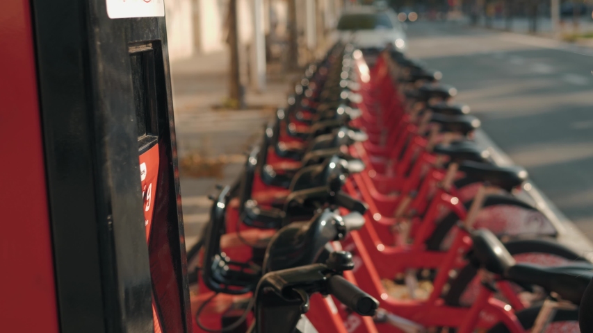 Row of red bicycles in a bike rack, available for rental on the streets of Barcelona, girl sharing take bike with card phone application