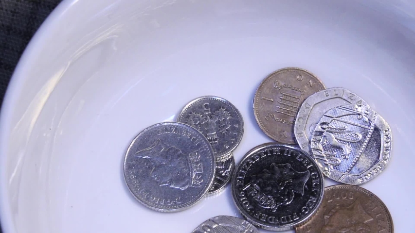 A  donation of assorted English UK coins are thrown into a white collection bowl in an act of charity. The money falls, rebounds and spins in slow motion. Royalty-Free Stock Footage #1033859717