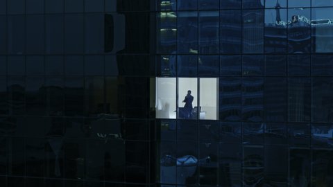 Aerial View Footage: From Outside into Office Building with Businessman Working and Looking out of the Window. Beautiful Retrieving Flying Away Shot of The Financial Business District Skyscrapers 
