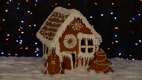 The hand-made eatable gingerbread house, little man, New Year tree, snow decoration, garland background illumination