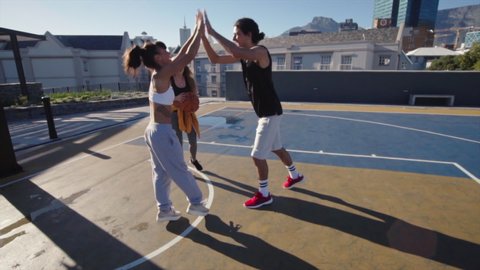 Group of friends playing street basketball and giving high five to one another. Man lifting woman to make a slam dunk while playing basketball game.
