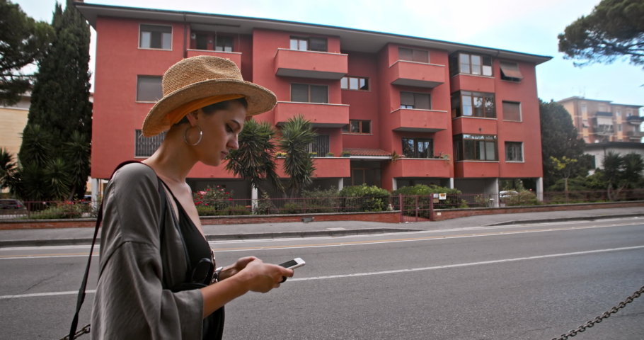 Side view sociable girl using a smartphone while walking in the city. Profile of pretty young woman on busy street traveling around beautiful Pisa, Italy.