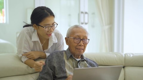 Elderly man using a laptop computer with his daughter on the sofa in living room at home. Shot in 4k resolution