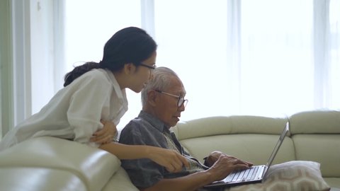 Old man working on a laptop computer with his daughter on the sofa in living room at home. Shot in 4k resolution