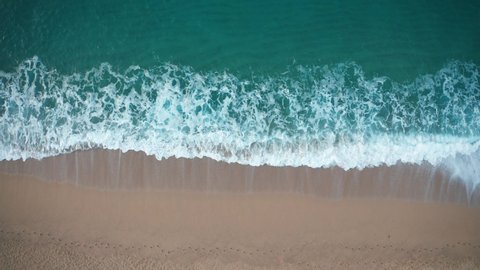 Drone view of beautiful seamless never ending footage while turquiose sea waves breaking on sandy coastline. Aerial shot of golden beach meeting deep blue ocean water and foamy waves