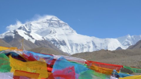 SLOW MOTION, CLOSE UP DOF: Colorful flags flutter in front of windswept Everest in the distance. Winds blowing across Mount Everest Base Camp sweep ice and snow off the mountaintop and make flags flap