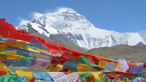 SLOW MOTION, CLOSE UP: Detailed shot of colorful prayer flags flapping in the wind blowing across the rocky foothills of Everest. Snow capped Mount Everest towers above the barren landscape in Tibet.