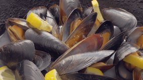 Chef mixes. Mussels with lemon juice. Cooking fresh seafood in a cast-iron skillet. Sash black shells opened. Wooden shovel and steam. Smooth video Rotation.