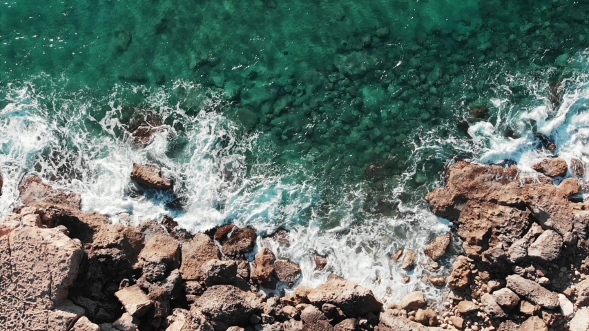 Aerial top view of large waves. Drone shot of rocky seashore. Sea coastline with extreme waves hitting rocks. Waves crashing rocky beach. Sea waves splashing