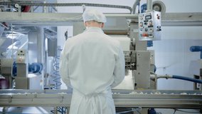 Young Male Food Conveyor Belt Employee Works at a Dumpling Factory. He Stands with His Back to Camera and Produce Manual Labour on the Line. He Wears White Sanitary Hat and Work Robe. - Powered by Shutterstock - Get 15% off with code: PIKWIZARD15