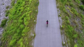 Aerial drone footage. A young athlete rides a healthy exercise bike. In the countryside on the embankment, there are beautiful views of the trees and the lake. Tracking shot
