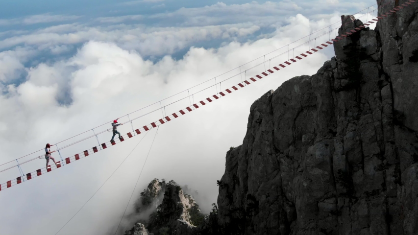 Person walking rope bridge, aerial view. Crossing over a suspension bridge in the mountains, walk above clouds. Extreme sport, risk, overtake, fear of height. Drone flight Royalty-Free Stock Footage #1033926446