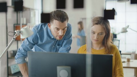 Female Specialist Works on Desktop Computer, Project Manager Stands Beside and gives Advice on Optimizing Workflow for Customer Experience Management. Modern Office with Diverse Team of Professionals