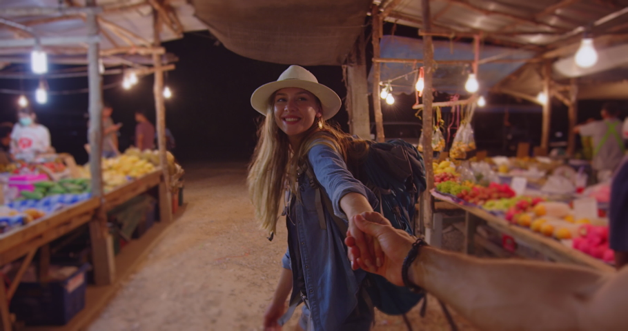 Young couple holding hands woman leading boyfriend. Walking towards asian food market in Thailand South East Asia. Pov slow motion, hand held.