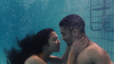 young couple kissing underwater in swimming pool enjoying intimate kiss romantic lovers submerged in water floating with bubbles in passionate intimacy