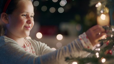 happy little girl decorating christmas tree with beautiful ornaments and baubles enjoying festive decorations at home on calm winter evening 4k footage