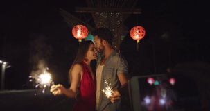 Young in love travel couple. Celebrating with fireworks with Chinese lanterns at night. Taking picture or video with smart phone. Slow motion, hand held. 