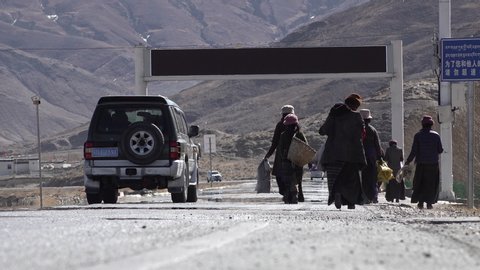 TIBET – JANUARY 2019: Local Tibetans walk on Chinese built main highway between Lhasa and Shigatse, get taken over by SUV jeep, poverty and contrast in Tibet