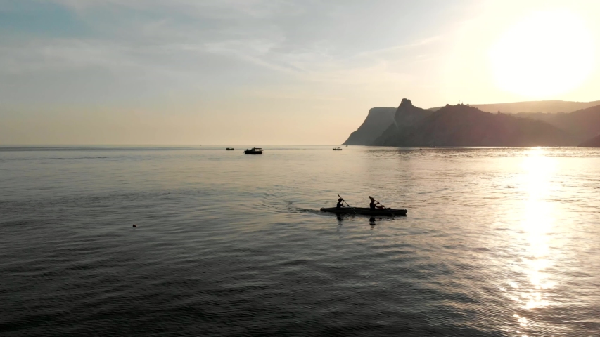 Aerial view of a kayak in the middle of the sea. Drone flight above two people kayakers paddling at sunset. Colorful sport kayak silhouette. Beautiful sea landscape at summer sunset.