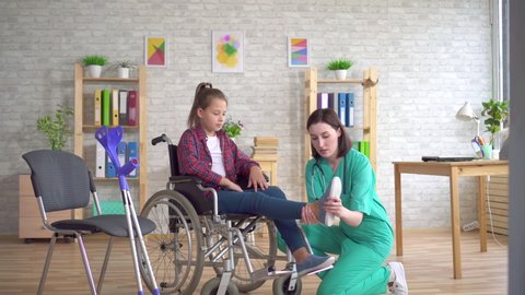doctor examines the leg of a teenage girl with a disability in a wheelchair