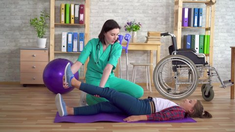 Physiotherapist in the rehabilitation center helps in warming up the legs of a teenage girl in rehabilitation after a spinal injury