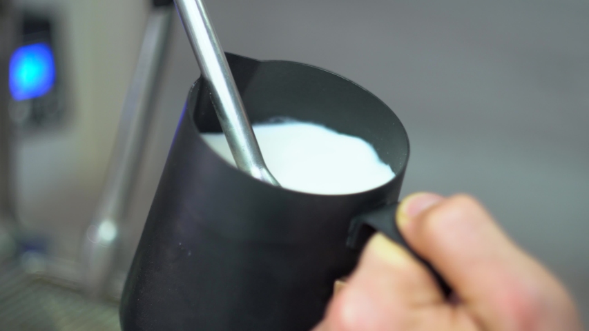 Whipping white milk in an blac coffee pot using a special tube of the coffee machine. Making coffee