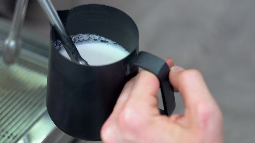 Whipping white milk in an blac coffee pot using a special tube of the coffee machine