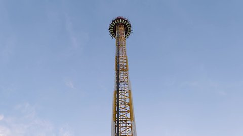Drop tower ride with exciting people on the seat, raising up, spinning and dropping at Carnival, amusement park or fun fair.