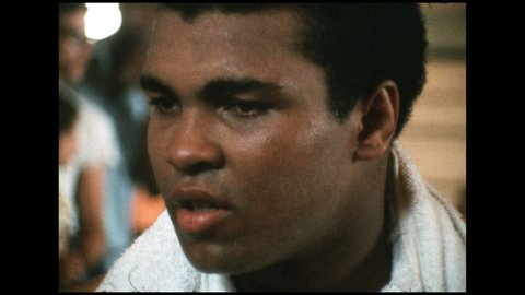 1970s: Muhammed Ali talks with interviewer outside boxing ring after match. Ali takes a drink from water bottle then continues with interview.