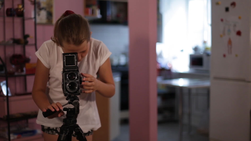 een girl looks into the mine of a medium format camera aimed at us, taking picture of you.