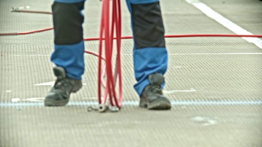 A man carrying a hose - wearing boots and big trousers