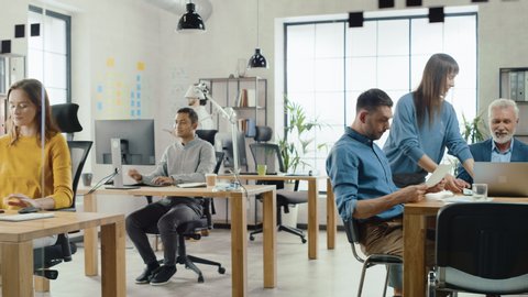 In the Stylish Modern Office: Diverse Group of Enthusiastic Business Marketing Professionals Use Computers, Have Meetings, Discussing Project Ideas, Brainstorming Startup Company Strategy