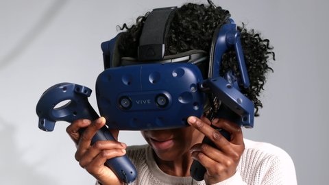 Montreal, Quebec / Canada - 03 05 2019: A curly african american woman uses htc vive vr headset and controllers for virtual reality game arcade center
