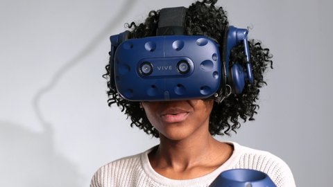 Montreal, Quebec / Canada - 03 05 2019: A curly african american woman uses htc vive vr headset and controllers for virtual reality game arcade center