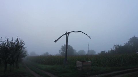 Still timelapse of a shadoof in the foggy sunrise. Some people are walking on the village path.