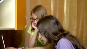 Two girls girlfriends, teenagers students sit together at the training table and use a laptop in the evening. they are cheerful and happy