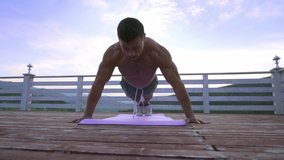 Handsome strong sporty male proficiently doing push ups exercises on yoga mat without shirt. Muscular dark haired guy workout in the evening outside