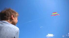 Closeup view of cte white kid playing colorful kite outdoor. Wide angle video footage of boy isolated at sunny blue sky background. Slow motion video footage.