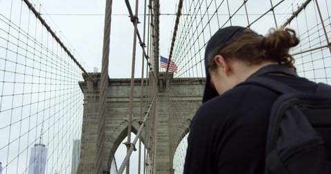 Handsome Male Model Looking Up To Beautiful Brooklyn Bridge With Waving American Flag In Slow Motion
