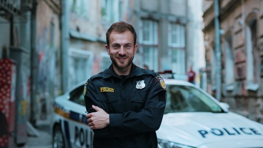 Smiling young man cops stand near patrol car look at camera 