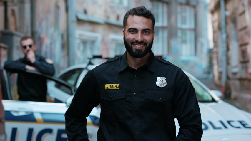Smiling young man cops stand near patrol car look at camera 
