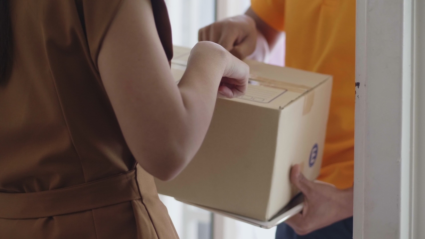 Young delivery Asian man holding a cardboard box while Asian young woman checking address on the box. Royalty-Free Stock Footage #1034015066