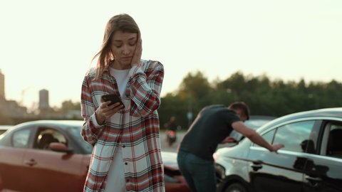 Portrait of confused young woman with smartphone worrying about the situation on road. Car crash, police in action. Girl searching something on mobile phone outdoors.
