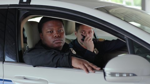 Close up portrait two men cops sitting in patrol car accepting emergence call enforcement talk look at camera officer police uniform auto safety security communication control policeman slow motion