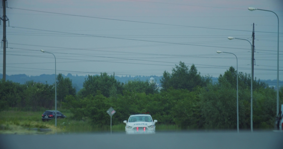 A police patrol car drives with its blue red lights flashing on the road in cloudy day. View of cops driving and patroling the city.