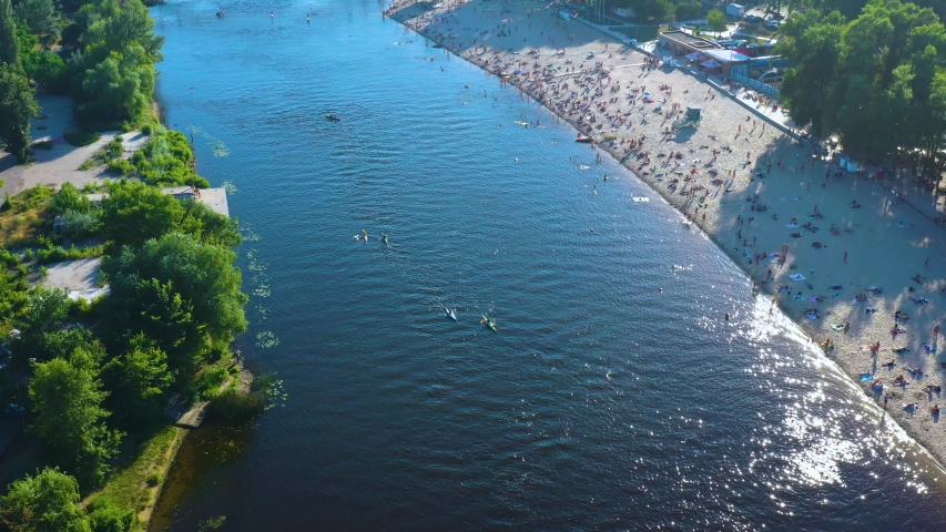 Aerial top view of unrecognizable people swimming and sunbathing on the bank of a river or lake on a sunny day