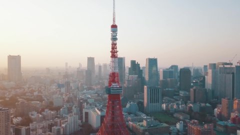 Drone aerial above Tokyo City panning around the iconic red Tokyo Tower surrounded by tall skyscrapers during a stunning sunset with blue and orange skies