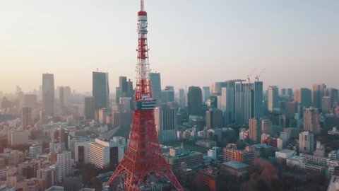 Drone aerial above Tokyo City panning around the iconic red Tokyo Tower surrounded by tall skyscrapers during a stunning sunset with blue and orange skies